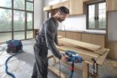A person wearing safety equipment uses a planer on wooden boards in a workshop.