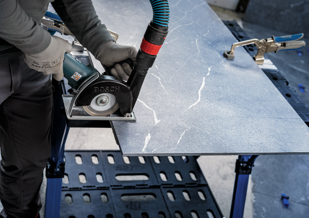 Person wearing safety equipment cuts a stone slab with a power saw.
