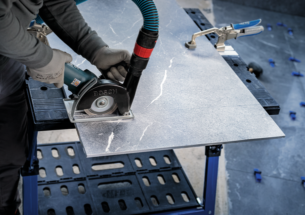 Person wearing safety equipment uses a circular saw to cut a large stone tile.