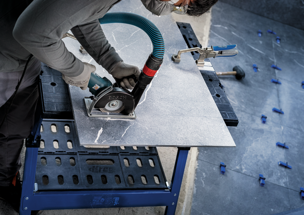 A person wearing safety equipment cuts a large tile panel with a circular saw.