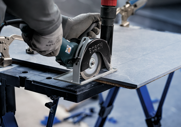 Person wearing safety equipment cuts a tile sheet with a circular saw.