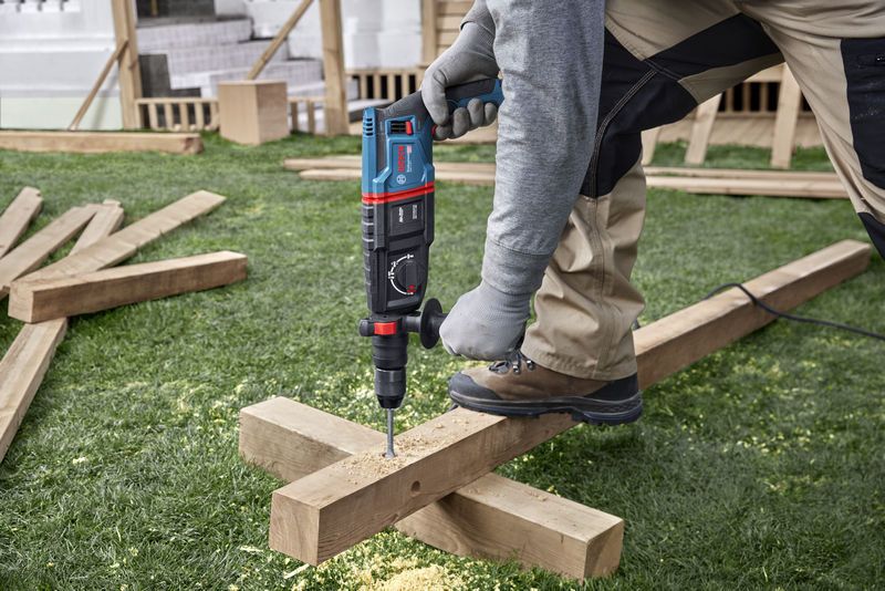 A person wearing safety equipment drills into a wooden beam at a construction site.