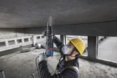 A person wearing safety equipment drills into a concrete ceiling on a construction site.