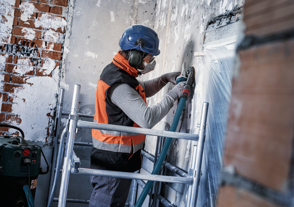 Object #200573501: 7743905_app_wide_1 Person wearing safety equipment grinds a concrete wall on scaffolding.