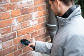 A person scans a brick wall with a material moisture meter.