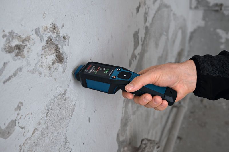 A person uses a material moisture meter to test a concrete wall.