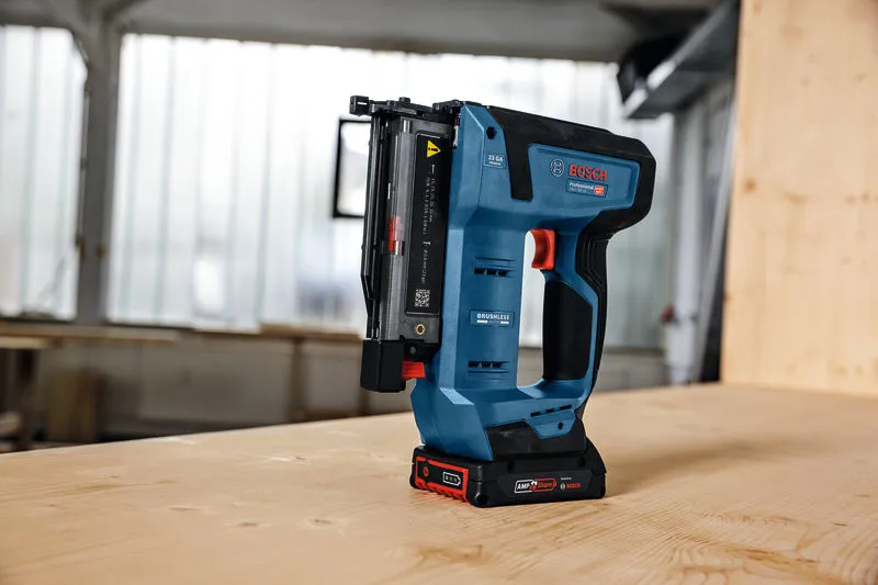 Cordless nail gun standing upright on a wooden table in a workshop.