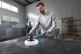 A person wearing safety equipment polishes a metal surface in an industrial workshop.