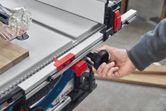Person adjusts table saw fence using a black knob in a workshop.