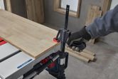 A person wearing safety equipment clamps a wooden board to a table saw.