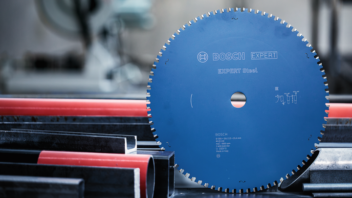 Object #200585208: 7557706_app_web_02 Circular saw blade positioned upright beside metal and plastic pipes in a workshop.