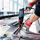 A person wearing safety equipment drills into a metal pipe at a construction site.