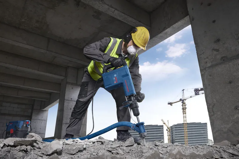 A person wearing safety equipment demolishes concrete with a demolition hammer.