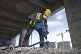 A person wearing safety equipment demolishes concrete with a demolition hammer.