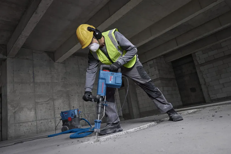 A person wearing safety equipment demolishes a concrete floor using a demolition hammer.