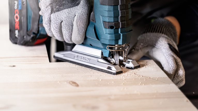 EXPERT ‘Wood 2-side clean’ T 308 B Jigsaw Blade 5-pc Person wearing safety equipment uses a cordless jigsaw to cut a wooden board.