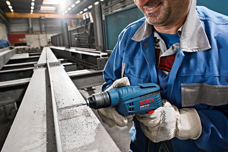 A person wearing safety equipment drills into a steel beam using a blue power tool.