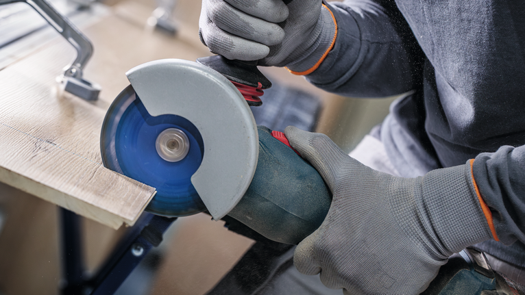 Person wearing safety equipment cuts wood with an angle grinder.