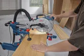 A person operates a mitre saw to cut a wood board in a workshop.