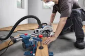 A person wearing safety equipment cuts wood flooring with a mitre saw.