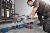 A person wearing safety equipment cuts a metal beam using a mitre saw.