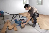 A person wearing safety equipment uses a mitre saw to cut wooden floor panels.