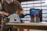 A person wearing safety equipment operates a dust extractor while cutting wood.
