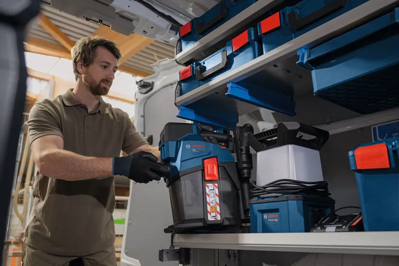A person wearing safety equipment organizes a cordless dust extractor in a work van.