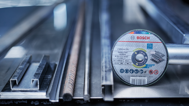 Cutting disc placed beside various metal rods and steel profiles on a workbench.
