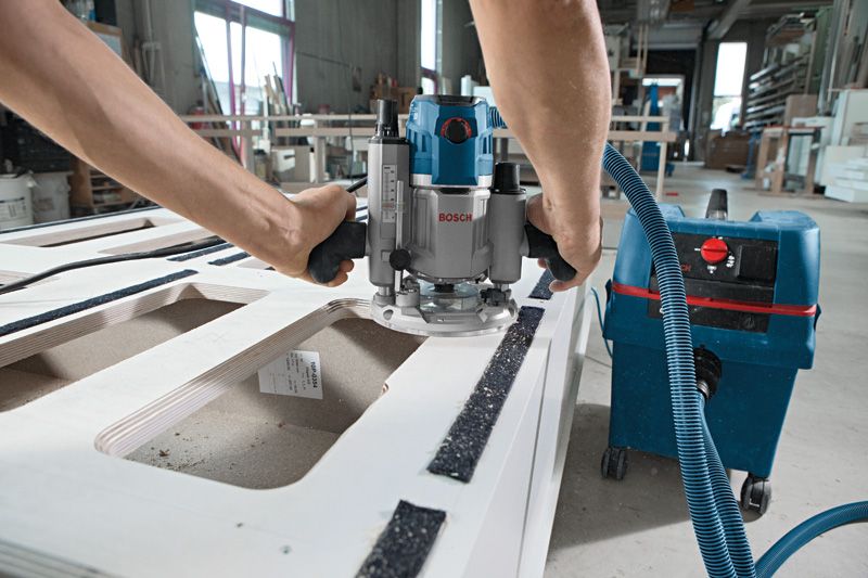 GOF 1600 CE A person uses a wood router connected to a wet dry extractor on a workbench.