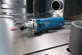 Straight grinder with a mounted pink abrasive stone resting on a metal surface.