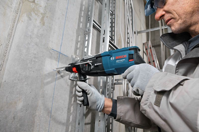 A person wearing safety equipment drills into a concrete wall along blue guide lines.