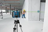 A person wearing safety equipment marks a wall using a green laser leveling tool.