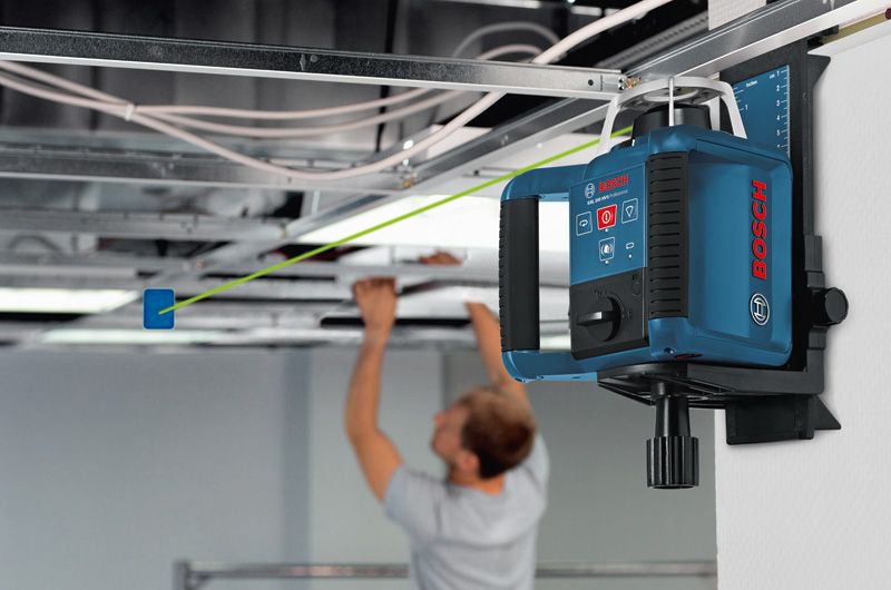 Laser leveling tool projects a green line as a person installs ceiling panels.