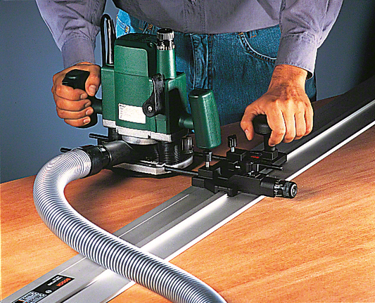 Worker guides a router along a metal rail on wood for precise cutting.